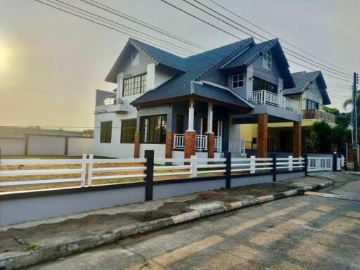 Exterior view of a modern two-story house with a large balcony and a fenced yard