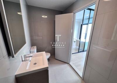 A modern bathroom with large mirror, sink, toilet, and glass door leading to another room