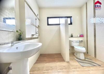 Modern and spacious bathroom with a shower area, toilet, and sink, featuring neutral tiles and a large window.