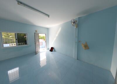 Spacious and empty living room with a blue-tiled floor, a large window, and a door opening to a balcony