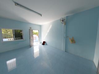 Spacious and empty living room with a blue-tiled floor, a large window, and a door opening to a balcony