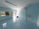 Spacious and empty living room with a blue-tiled floor, a large window, and a door opening to a balcony