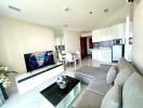 Modern living room with a gray sectional sofa, flat-screen TV, dining area, and open kitchen