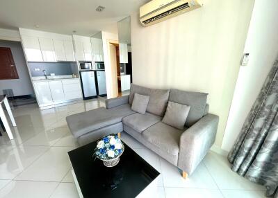 Living room with gray sectional sofa, glass coffee table, and modern kitchen in the background