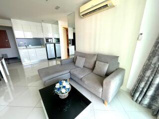 Living room with gray sectional sofa, glass coffee table, and modern kitchen in the background