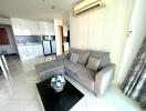 Living room with gray sectional sofa, glass coffee table, and modern kitchen in the background