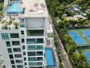 Aerial view of a modern multi-story building with multiple pools and tennis courts nearby.