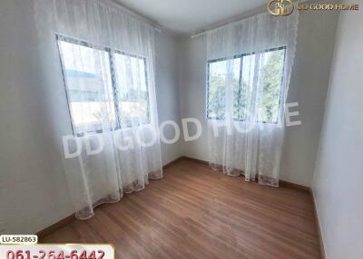 A bright and airy bedroom with wooden flooring and two windows adorned with white sheer curtains.