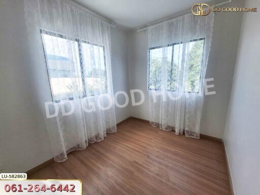 A bright and airy bedroom with wooden flooring and two windows adorned with white sheer curtains.