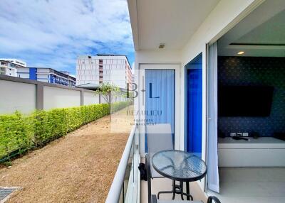 Outdoor balcony with table, chairs, and a view of a green hedge and neighboring buildings