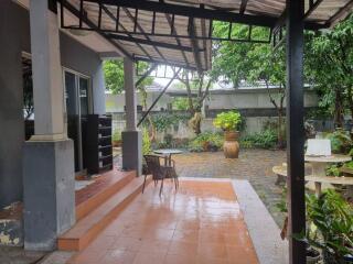 Covered outdoor patio area with a small table and chairs, providing a view of a lush garden.