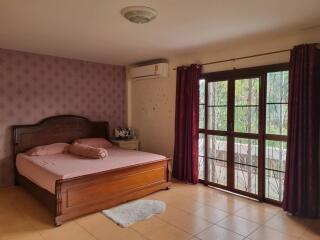A spacious bedroom with a wooden bed, large windows, and air conditioning