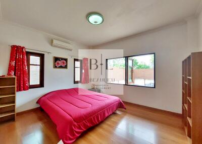 Cozy bedroom with a red bedspread, wooden floor, and large windows