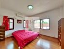 Cozy bedroom with a red bedspread, wooden floor, and large windows