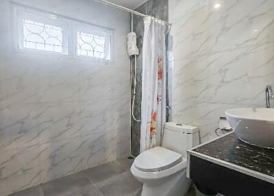 Clean and modern bathroom with marbled walls, vanity sink, toilet, and shower area with curtain