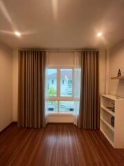 Room with wooden flooring, large window with curtains, and shelf