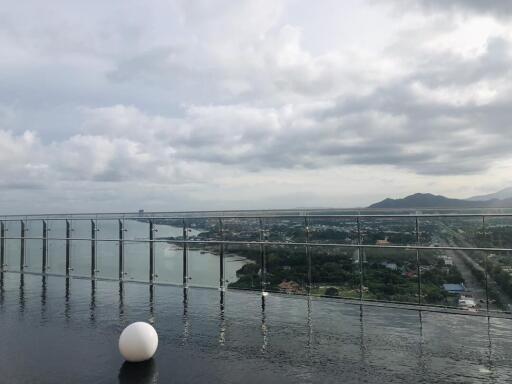 Balcony with glass railing overlooking a scenic landscape with mountains and a body of water