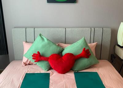 Neatly made bed with green pillows, red heart pillow, and modern decor