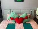 Neatly made bed with green pillows, red heart pillow, and modern decor