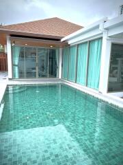 Outdoor swimming pool with surrounding patio and large glass doors leading to interior