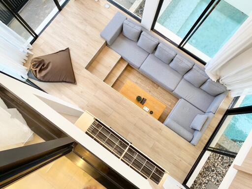 Modern living room with gray sectional sofa, wooden floor, large windows, and indoor pool view