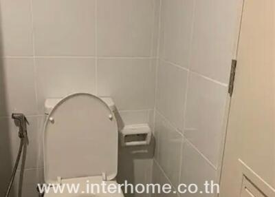 Bathroom with white tile walls, toilet, bidet spray, and a wall-mounted toilet paper holder