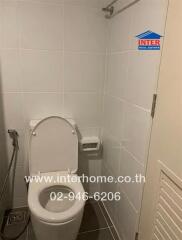 Bathroom with white tile walls, toilet, bidet spray, and a wall-mounted toilet paper holder