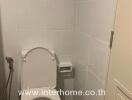 Bathroom with white tile walls, toilet, bidet spray, and a wall-mounted toilet paper holder