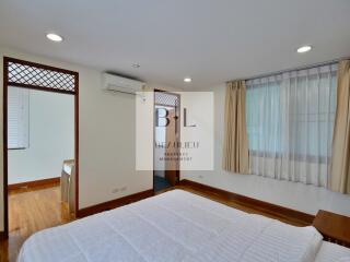 Spacious bedroom with bed, air conditioner, and large windows with curtains