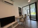 Living area with TV, dining table, chairs, and sliding glass doors leading to a balcony