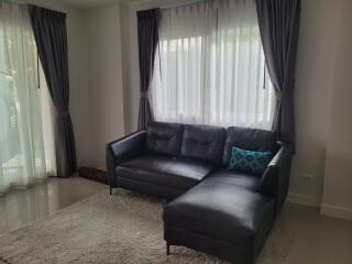 Living room with a dark leather sectional sofa, white curtains, and a soft rug