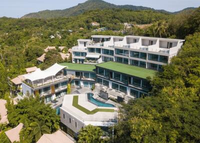 Aerial view of a modern multi-level residential building with green rooftops surrounded by lush greenery and hills.