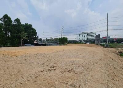 Open land area with trees, buildings, and electric lines in the background