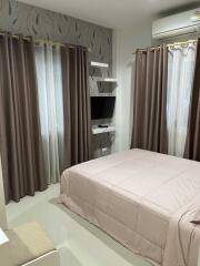 A modern bedroom with brown curtains, a wall-mounted TV, and a bed with a light-colored comforter.