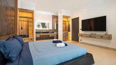 Modern bedroom with large bed, built-in wardrobe, wall-mounted TV, and ensuite bathroom