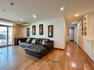 living room with black sectional sofa, decorative wall art, and wooden flooring