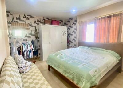 A spacious bedroom with a double bed, sofa, wardrobe, and window with curtains.