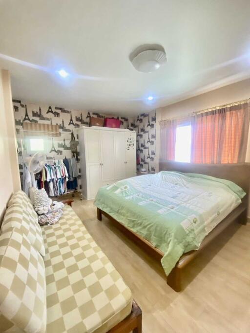 A spacious bedroom with a double bed, sofa, wardrobe, and window with curtains.