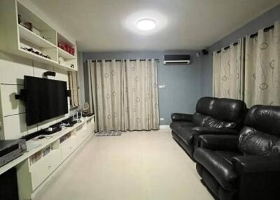 Modern living room with black leather sofas, wall-mounted TV, and white shelving unit