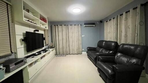 Modern living room with black leather sofas, wall-mounted TV, and white shelving unit