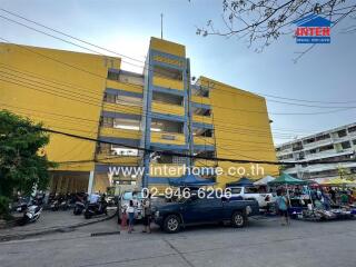 Front view of a building with nearby parked vehicles and market stalls