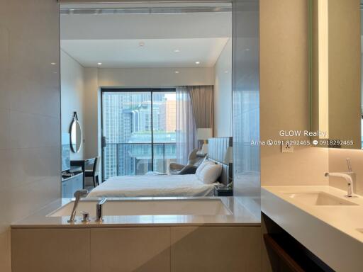 Modern bedroom with large window and city view, adjacent to a bathroom with transparent partition and bathtub