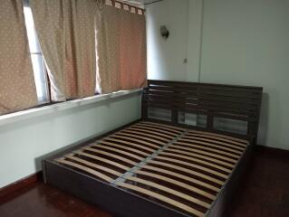 Bedroom with a wooden bed frame and window with curtains