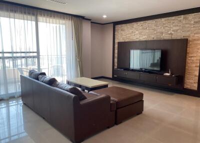 Contemporary living room with brown sectional sofa, wall-mounted TV, and large windows with curtains
