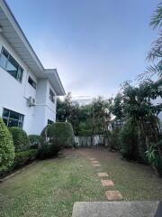 Green garden area with path, shrubs, and trees next to a two-story house