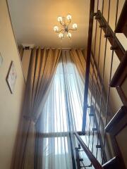 Staircase with chandelier and large window with curtains