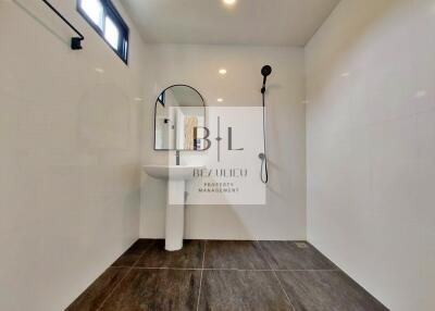 Modern bathroom with white walls, dark floor tiles, and a round mirror