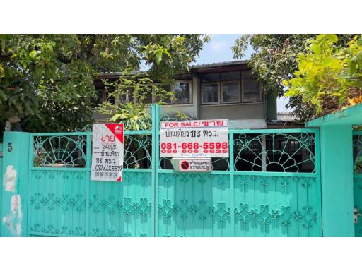 Front view of a residential building with a turquoise gate and For Sale signs