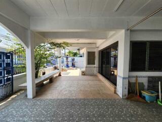 Covered outdoor area with tiled flooring, seating bench, and surrounding greenery