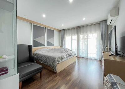 Modern bedroom with large bed, armchair, and TV, featuring wooden floor and ample natural light